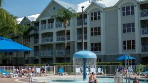 hotel exterior with pool in front and people swimming in the pool